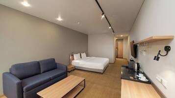 A modern hotel room with a sofa, a bed, a small table, and a kitchenette area.