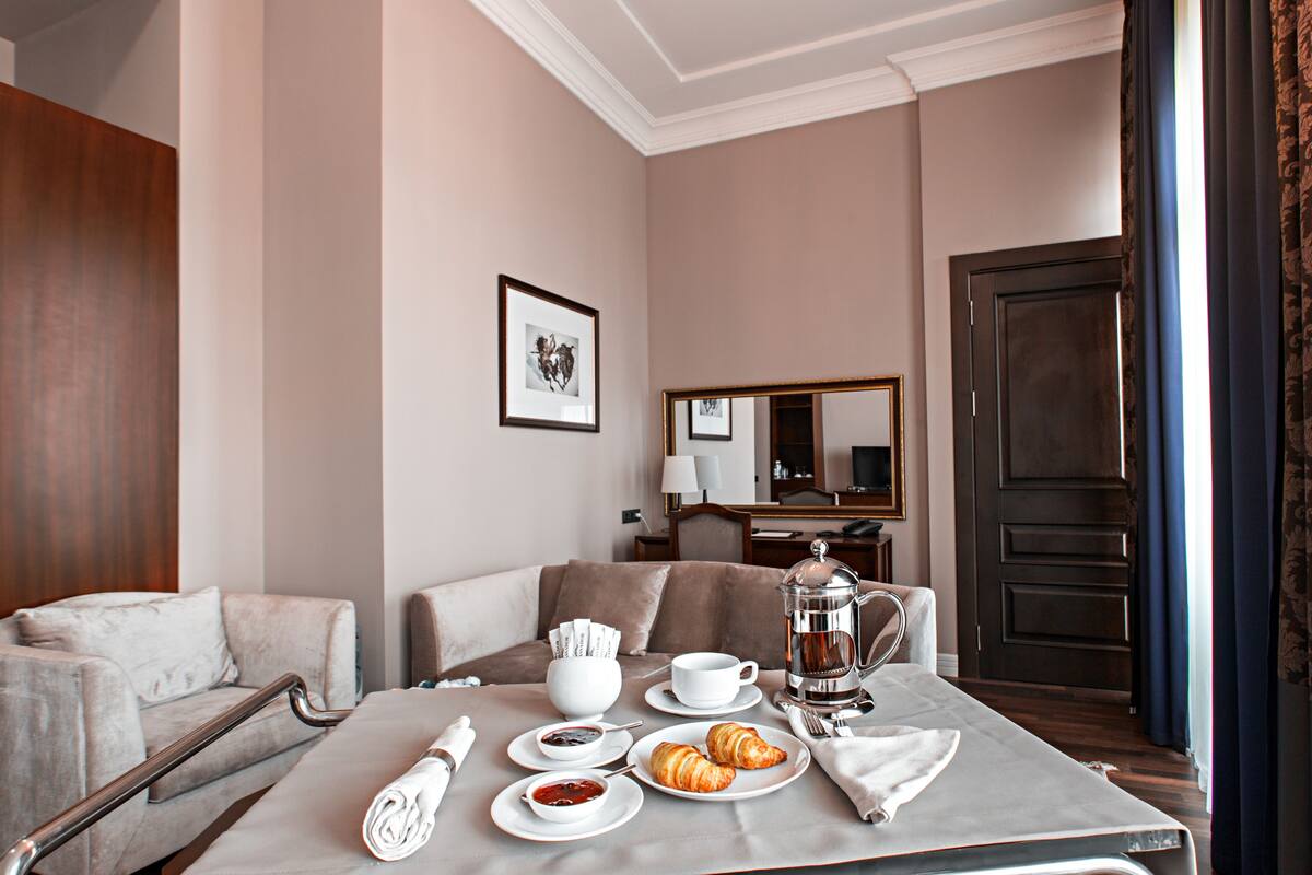 Habitación de hotel con una mesa de comedor preparada para el desayuno, un sofá, una cama y un espejo grande en la pared.