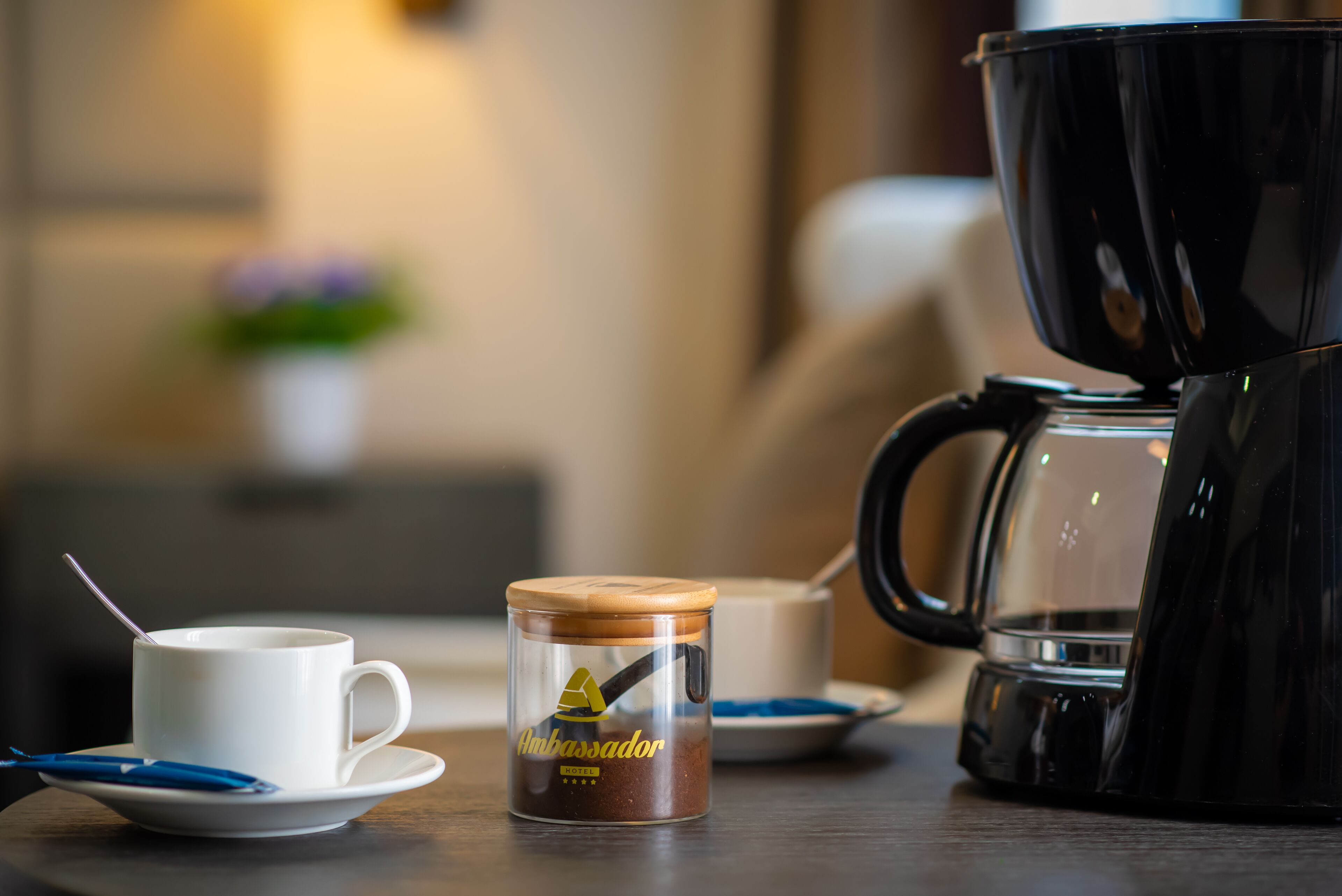 Uma cafeteira, uma chávena, uma colher e um recipiente com café sobre uma mesa.
