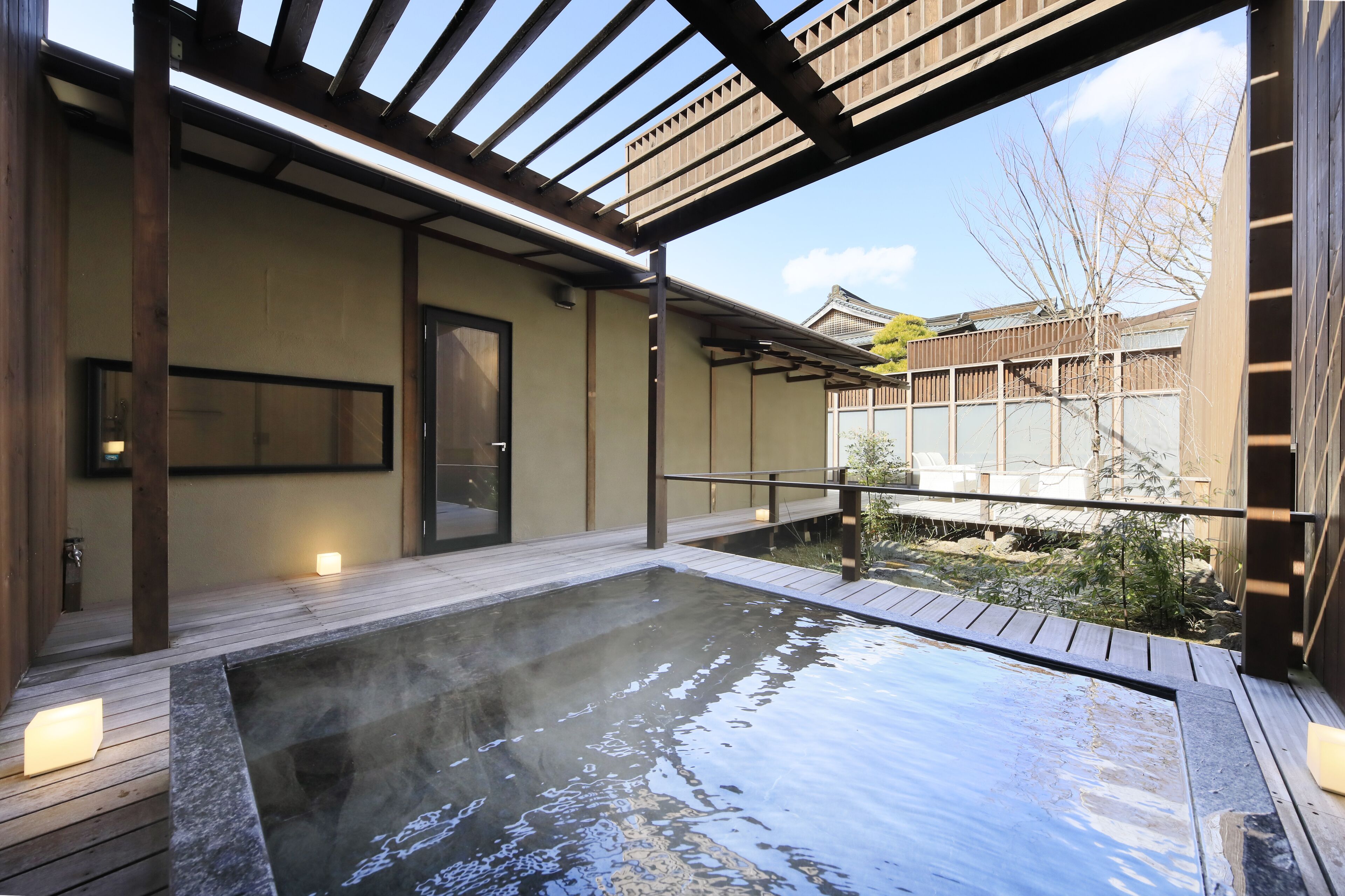 A hot spring area with wooden decking, a stone basin, and a view of a traditional building in the background.