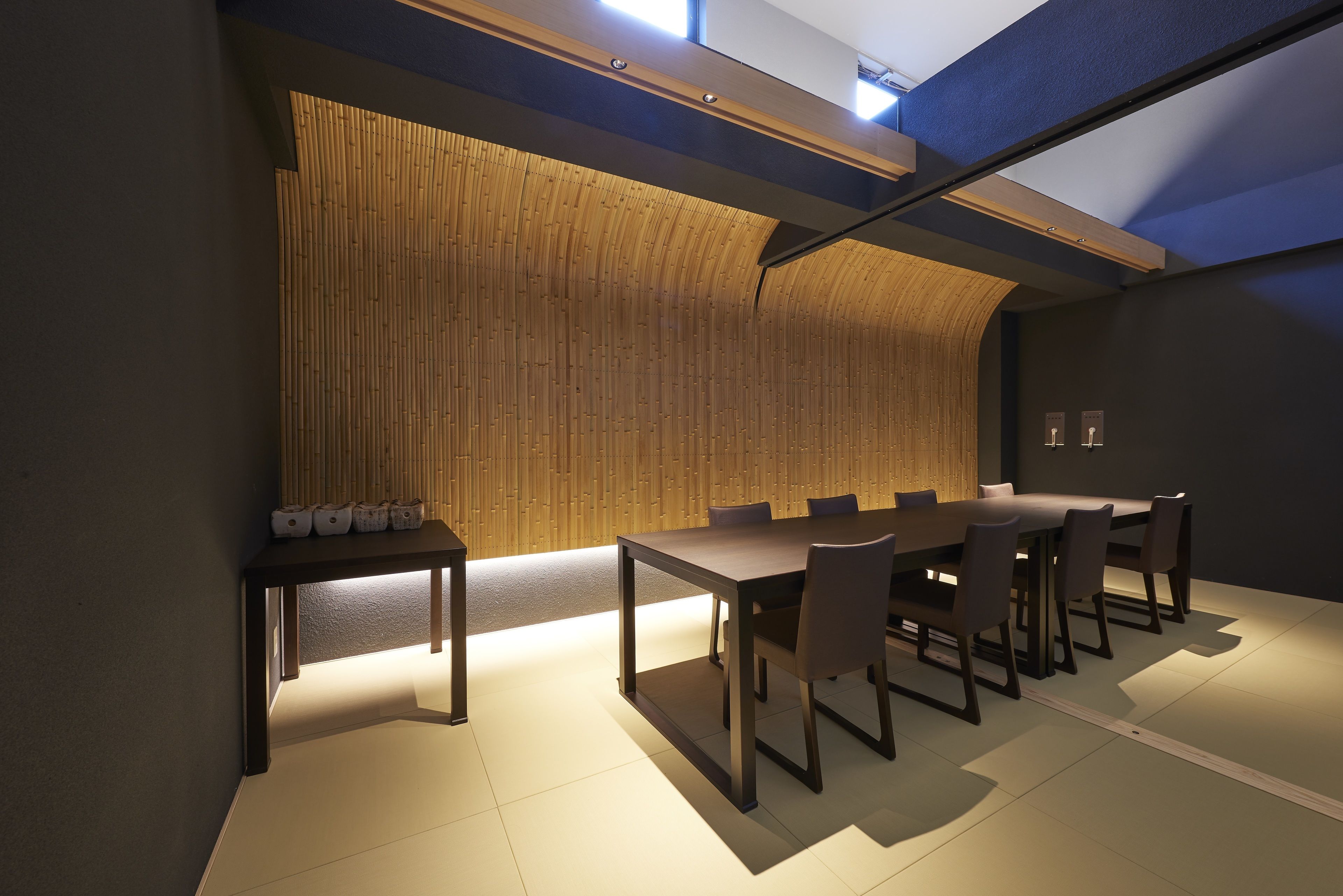 A modern dining area with a long table and chairs, a wooden wall, and a ceiling with skylights.