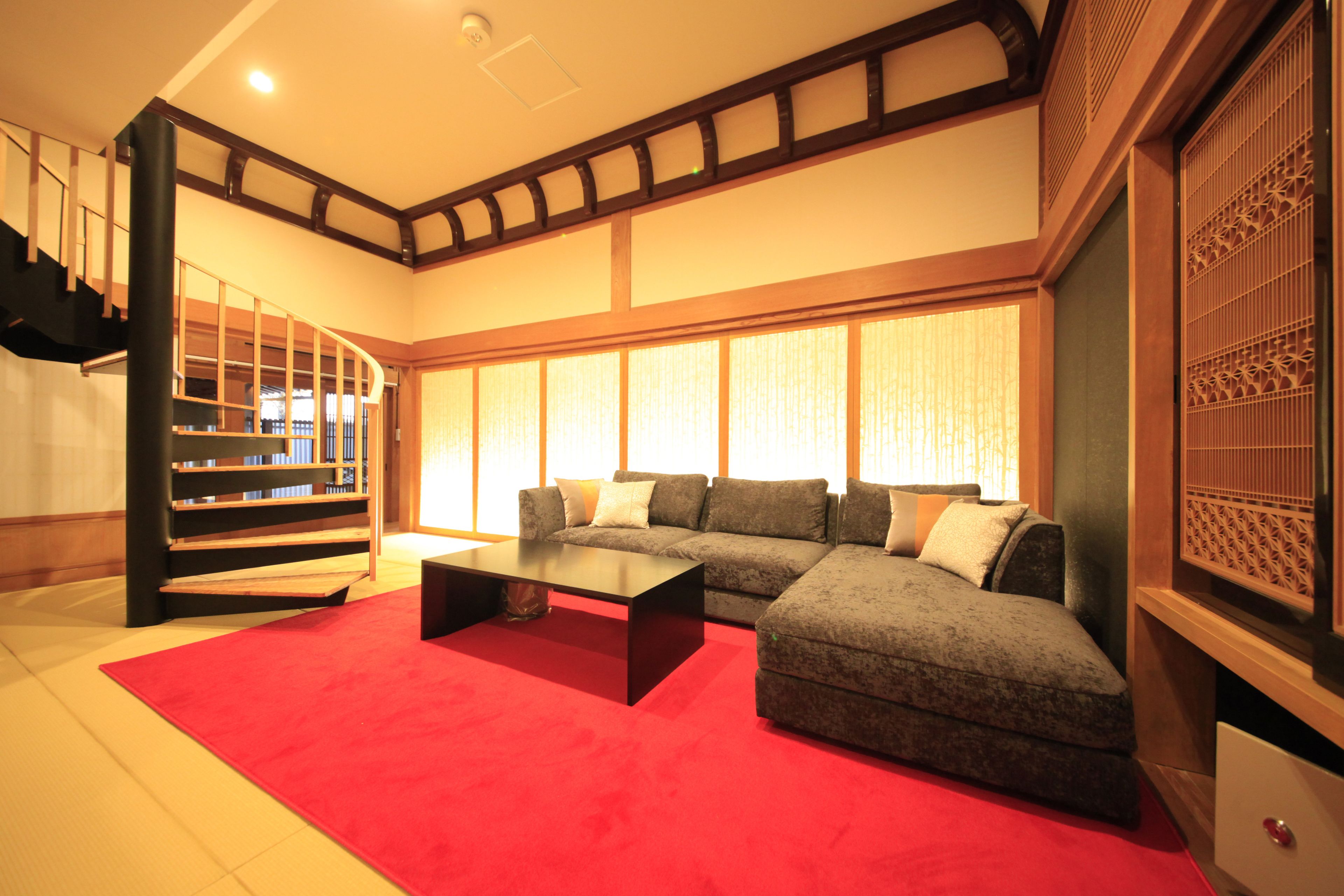 Ein Wohnzimmer mit einem Ecksofa, einem roten Teppich, einem schwarzen Couchtisch und einer Treppe mit Holzbalken.