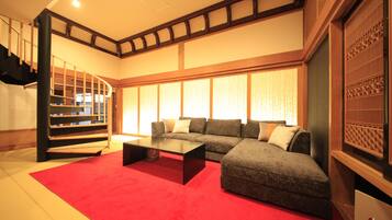 Ein Wohnzimmer mit einem Ecksofa, einem roten Teppich, einem schwarzen Couchtisch und einer Treppe mit Holzbalken.