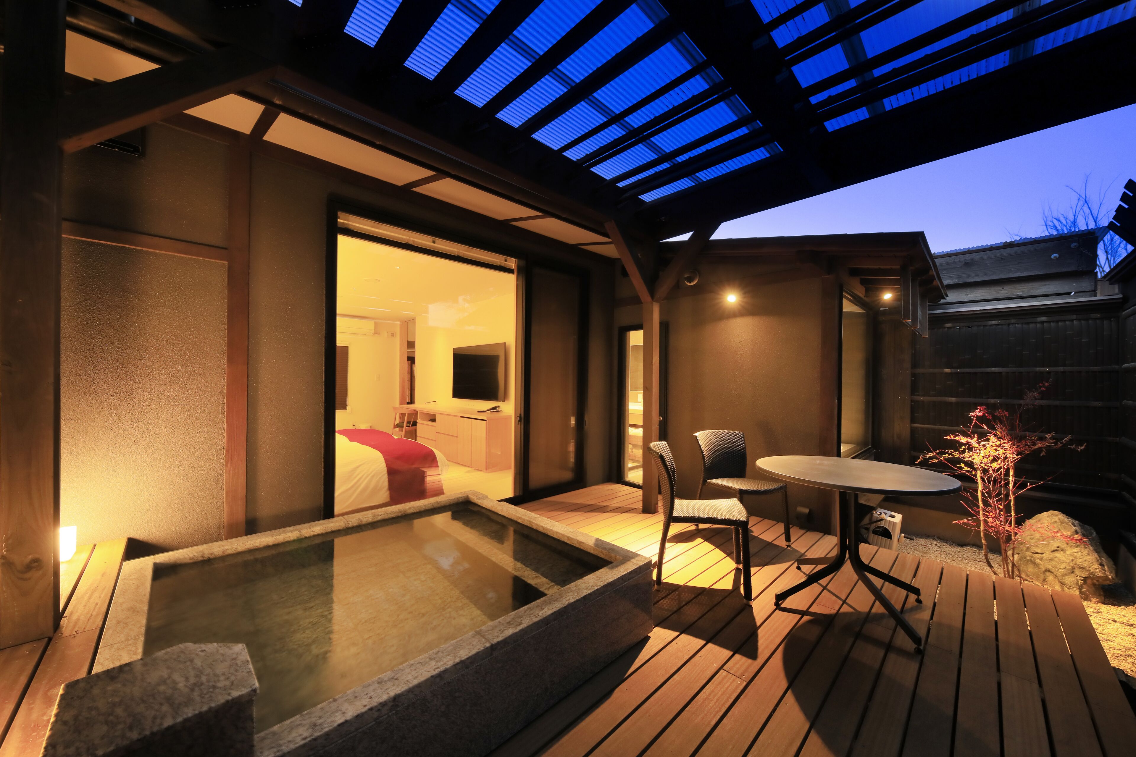 Ein moderner Außenbereich mit Whirlpool, einer Holzterrasse und einem Pavillon aus Glas, sowie einem kleinen Tisch und Stühlen.