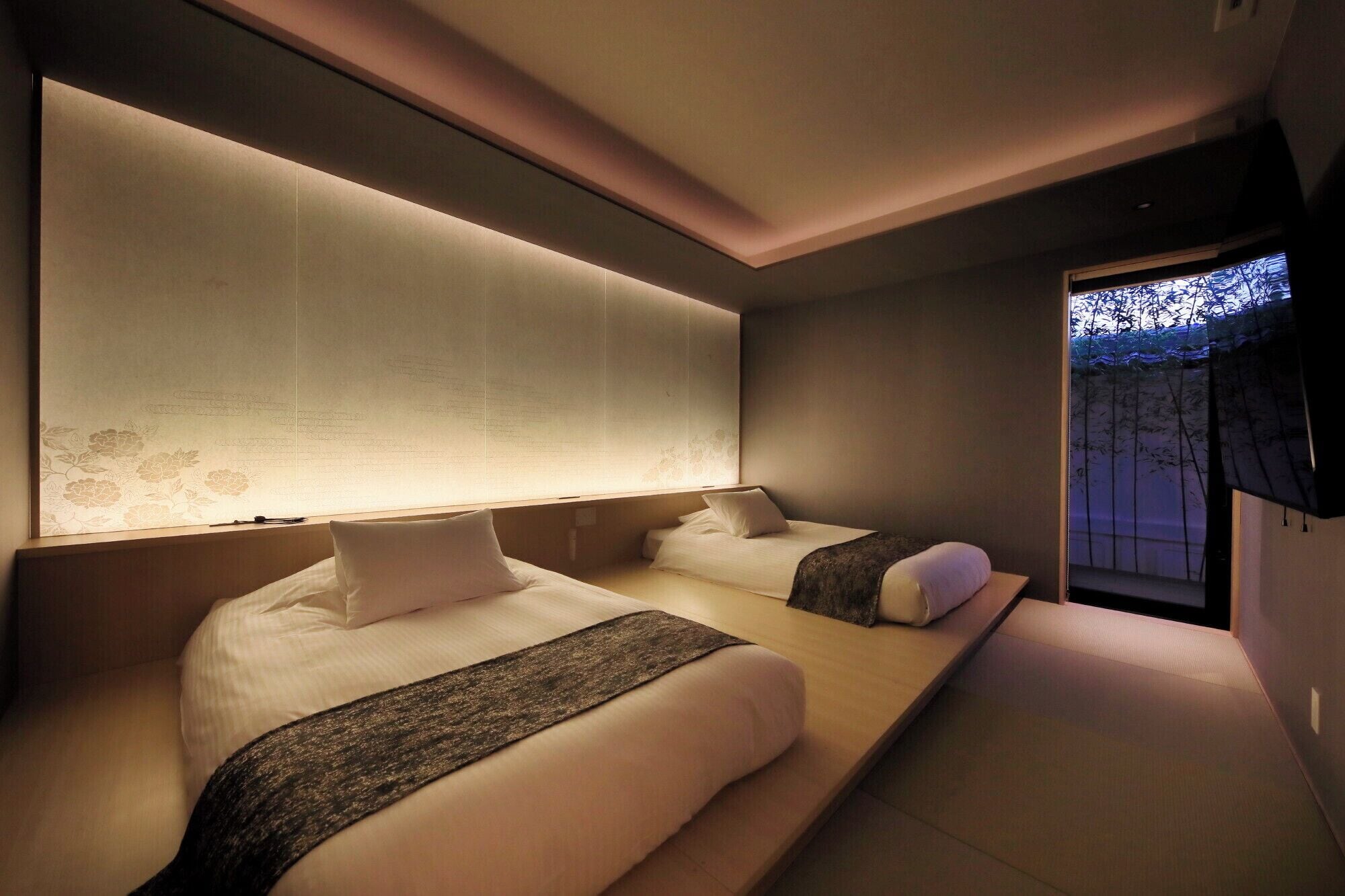 A modern hotel room with two beds, a large wall with a floral pattern, and a view of bamboo outside.