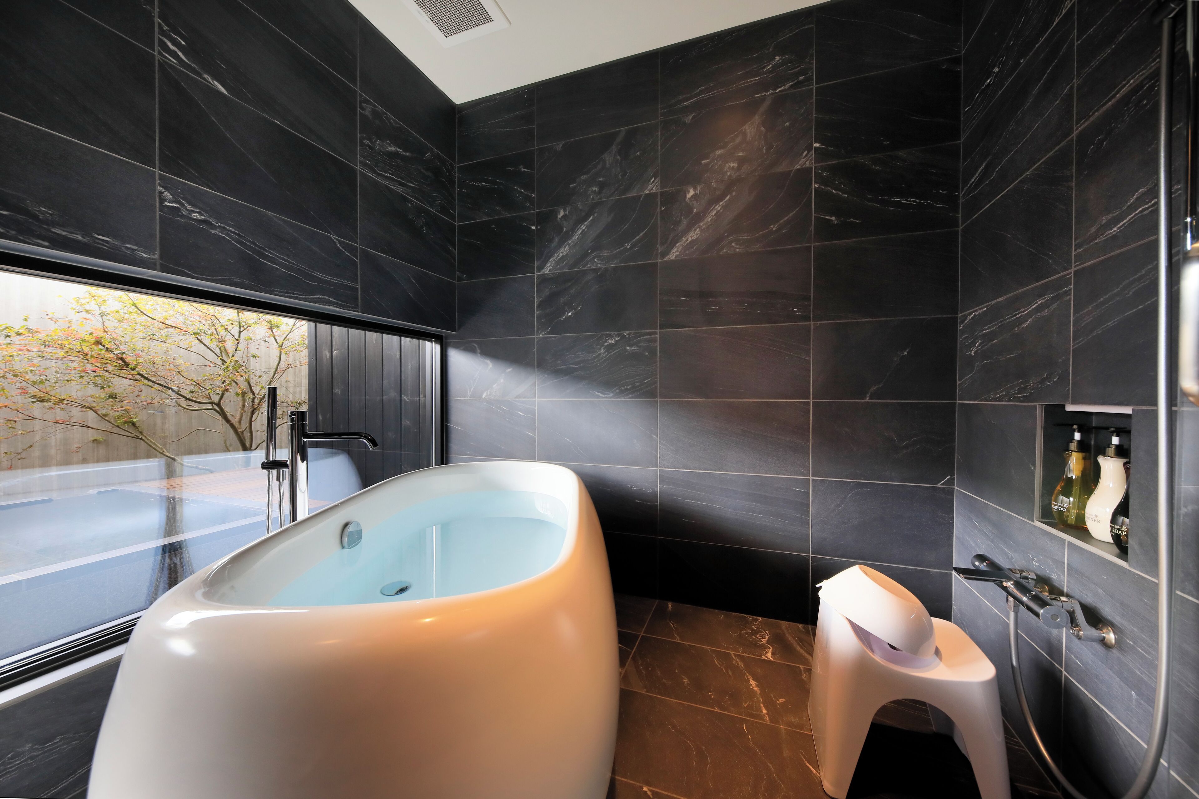 A modern bathroom with a large bathtub, a small stool, and a shower area.