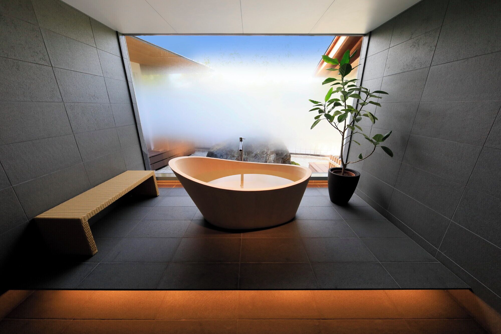 A modern bathroom with a freestanding bathtub, a bench, and a potted plant.