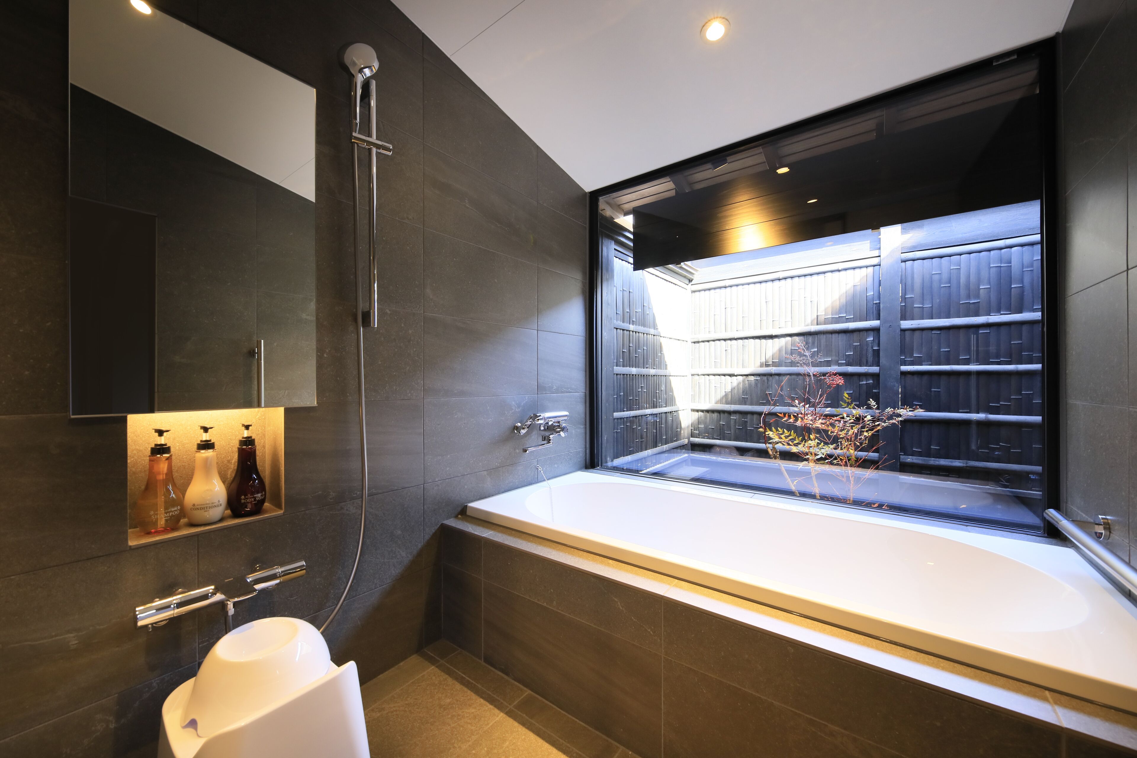 A modern bathroom with a large bathtub, a glass-enclosed shower, and a built-in shelf with toiletries.