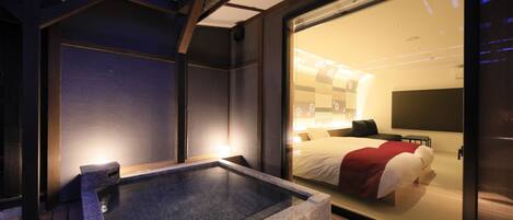 Una habitación moderna con un jacuzzi, una cama con una manta roja y un ventanal grande.