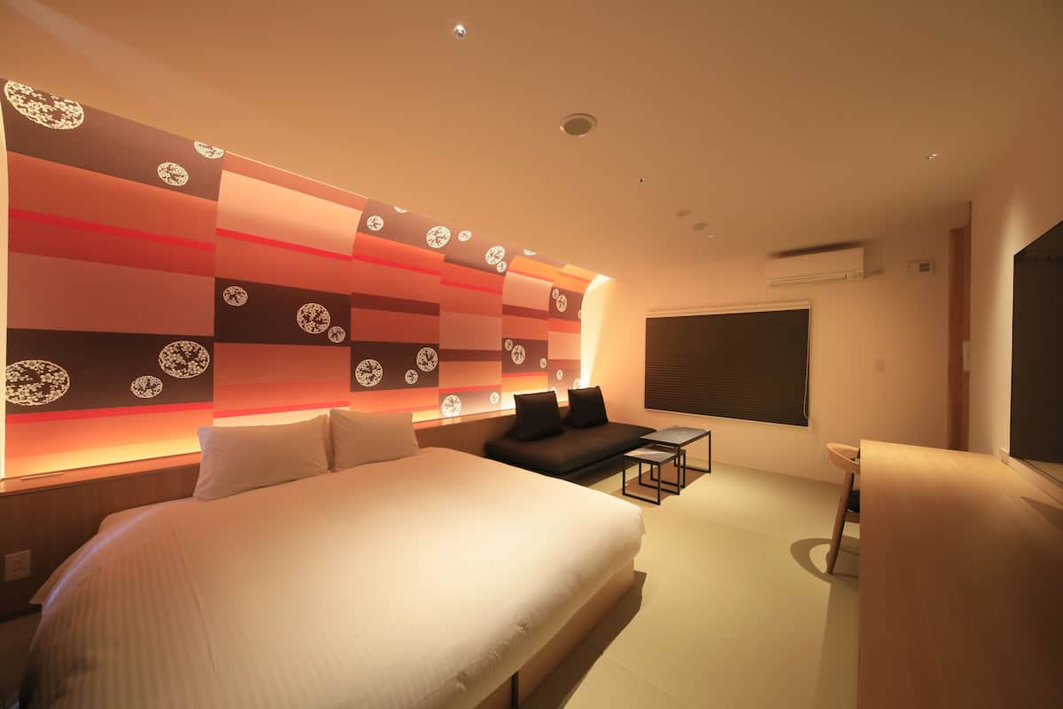 Ein modernes Hotelzimmer mit einem großen Bett, einer Couch, einem kleinen Tisch und einem an der Wand befestigten Fernseher.