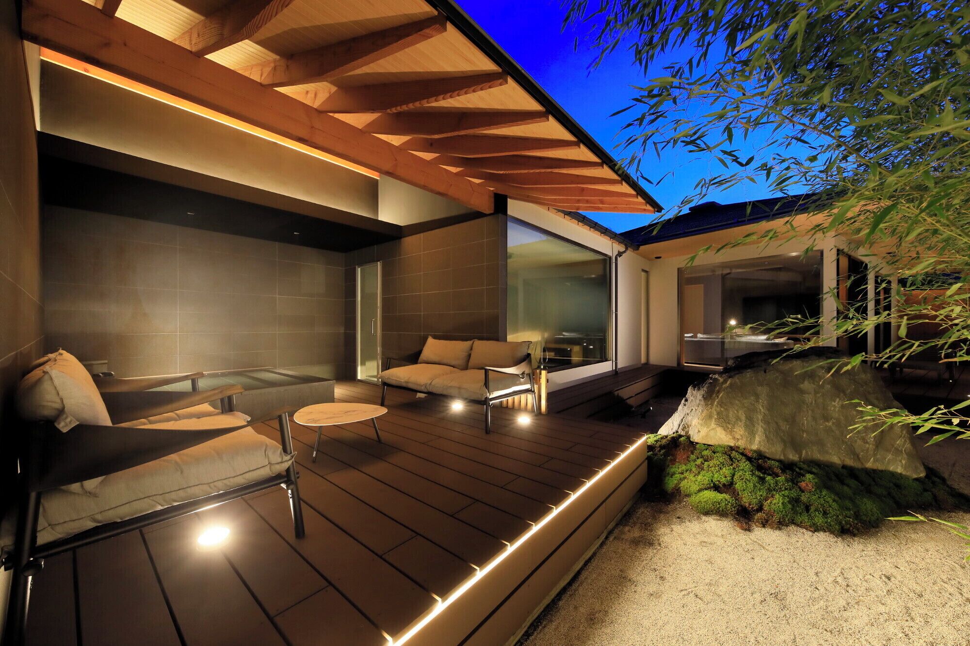 A modern outdoor deck with a hot tub, seating area, and a view of a bamboo garden.