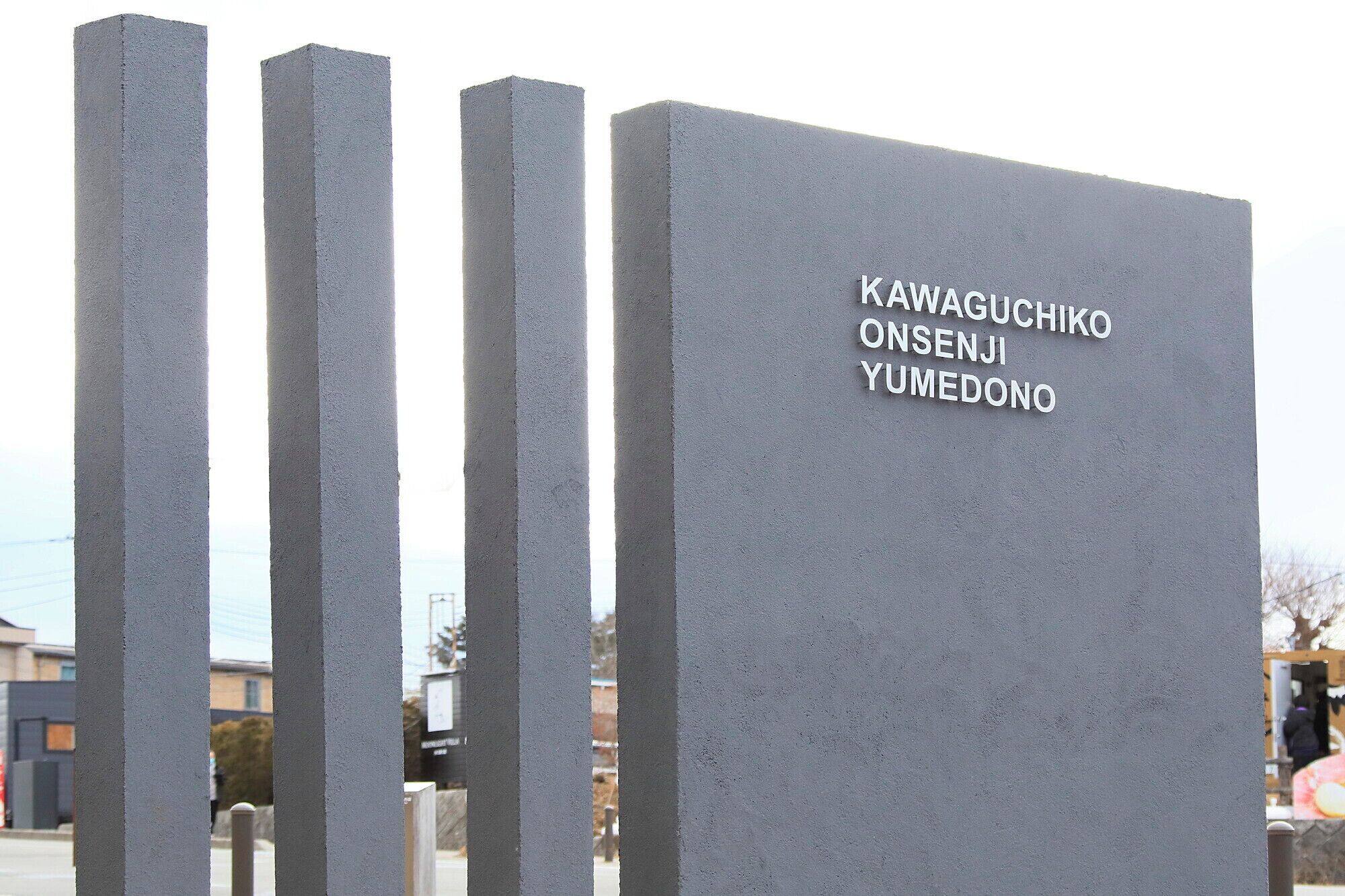 Un monumento de concreto con la inscripción "Kawaguchiko Onsenji Yumedo" en un espacio público.