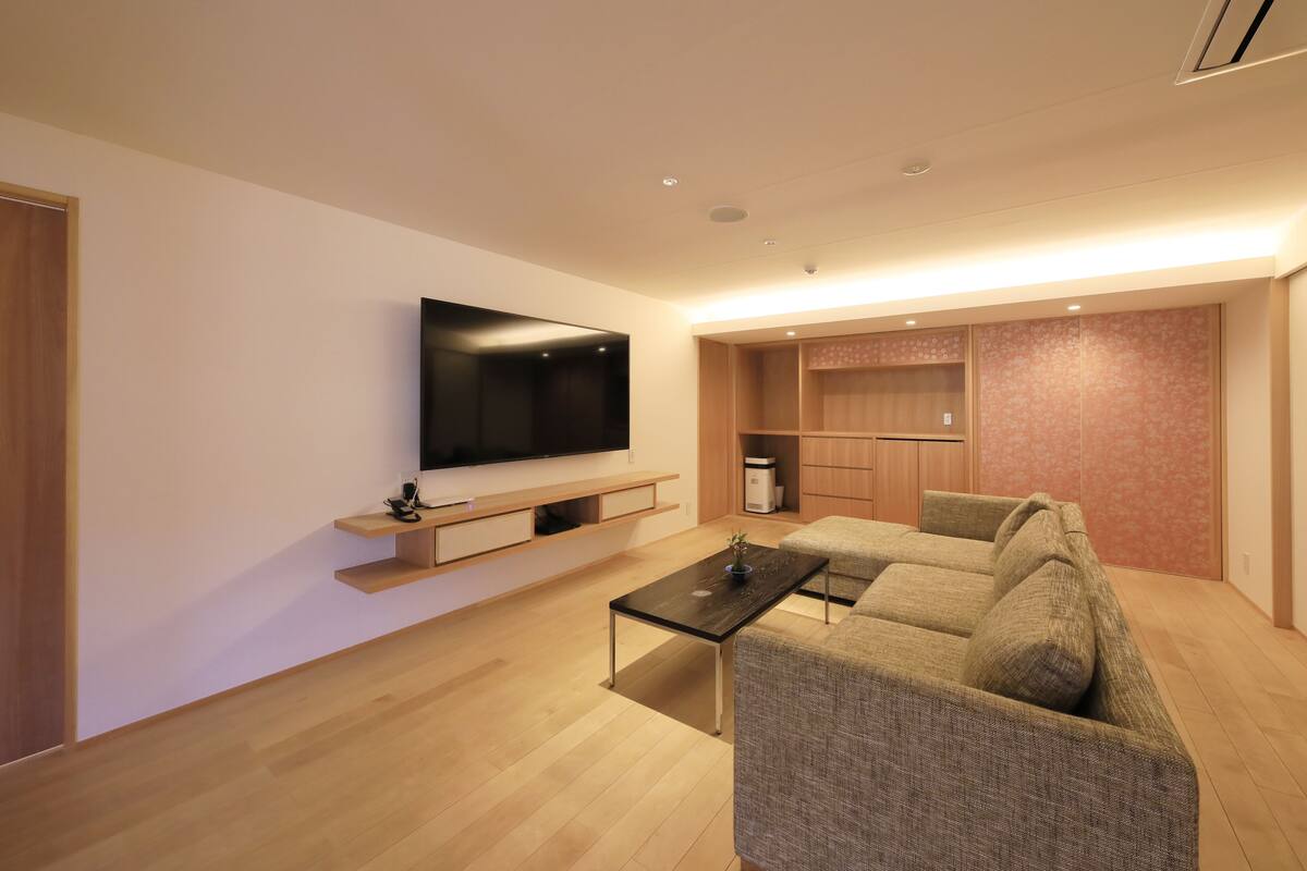 Ein modernes Wohnzimmer mit Flachbildfernseher, einer Couch, einem Couchtisch und einer Küchenzeile im Hintergrund.