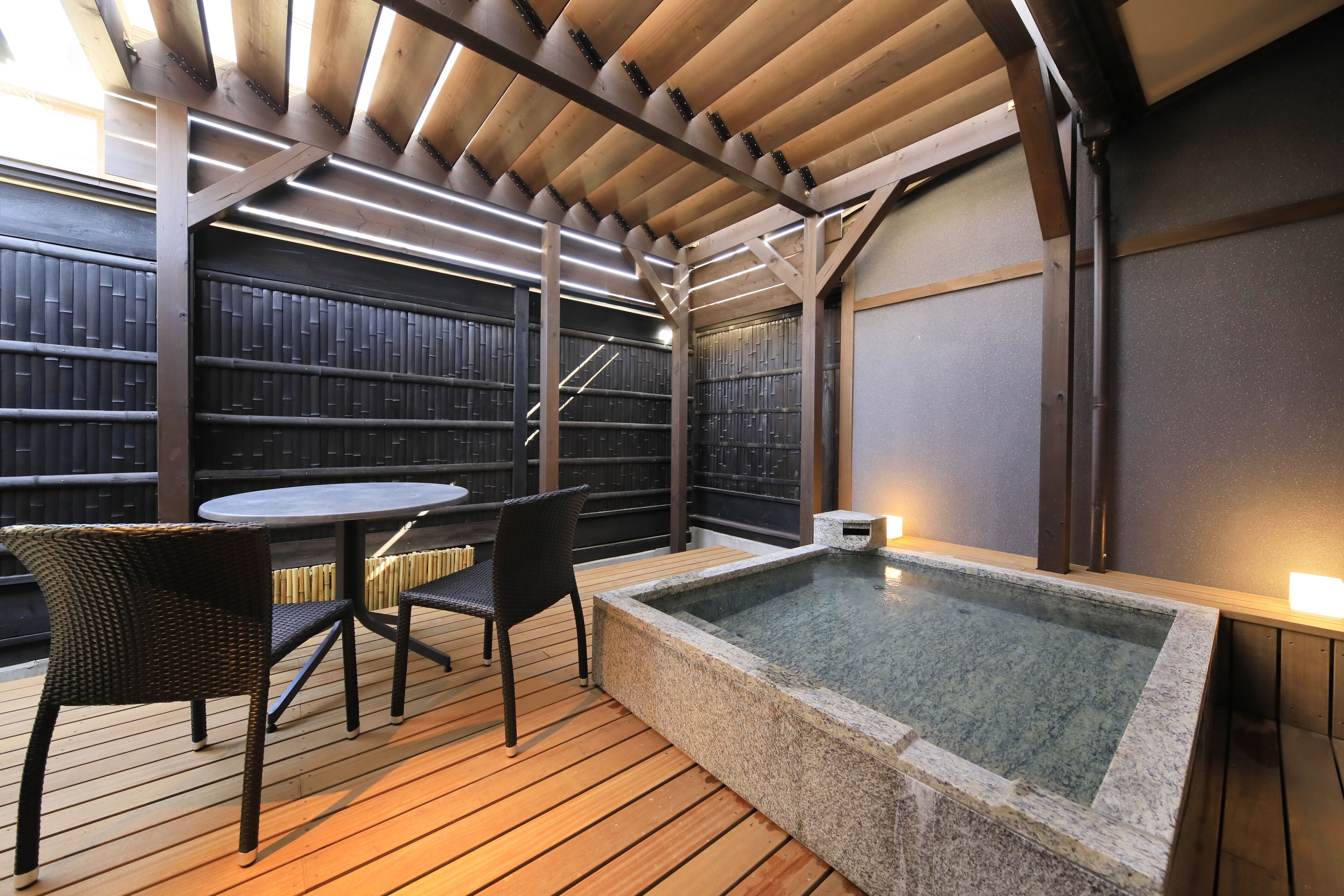 A wooden deck with a hot tub, two wicker chairs, and a table.