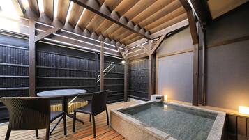 A wooden deck with a hot tub, two wicker chairs, and a table.