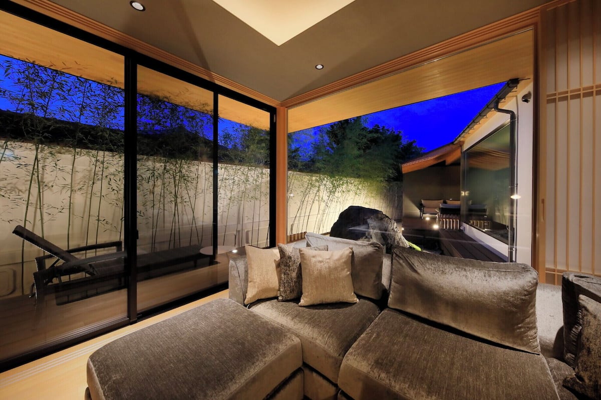 Ein modernes Interieur mit einer Couch, großen Fenstern und Blick auf Bambus draußen.