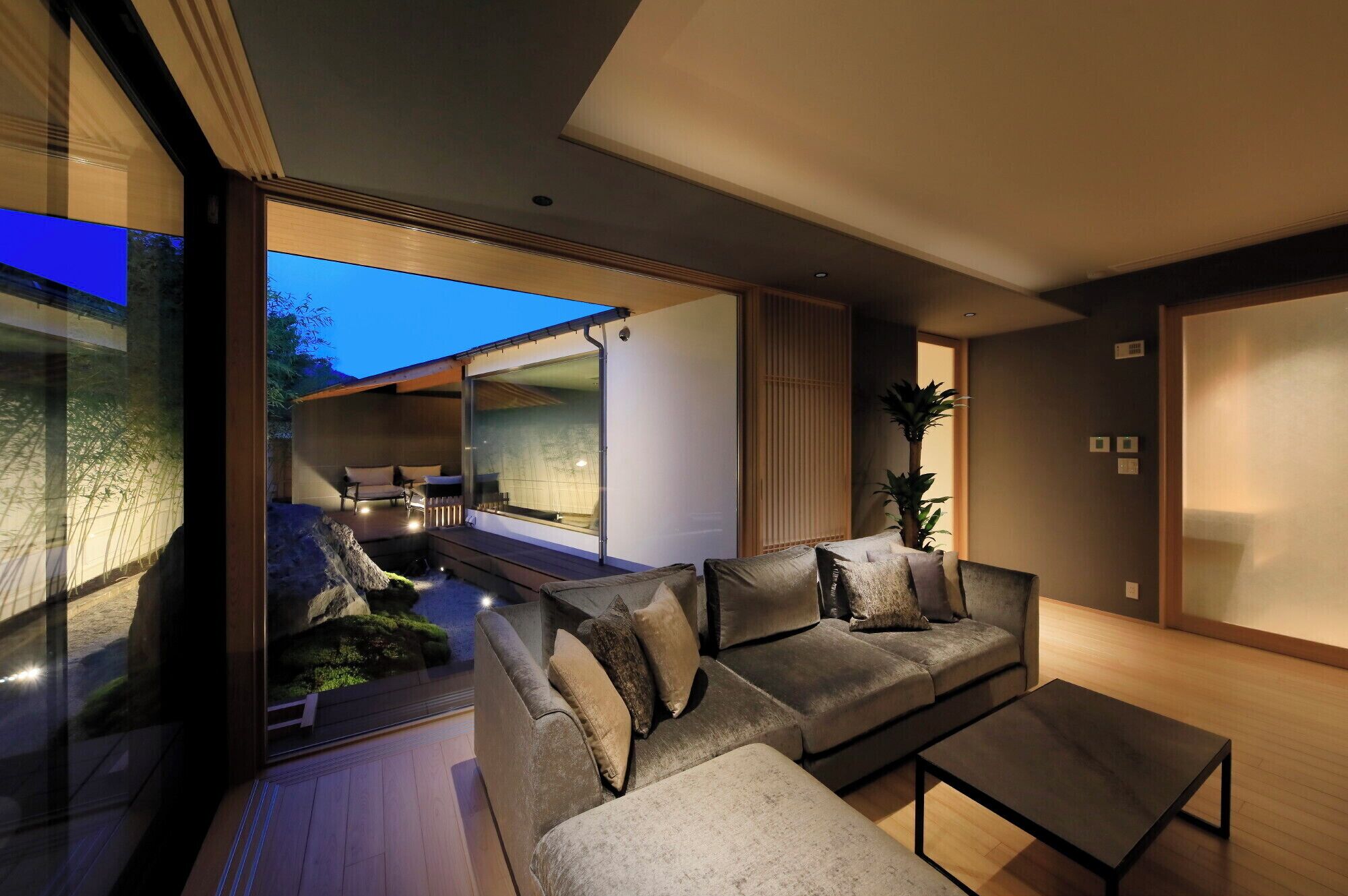 Un interior moderno con un sofá, una mesa de centro y un muro de cristal con vistas a una terraza exterior.