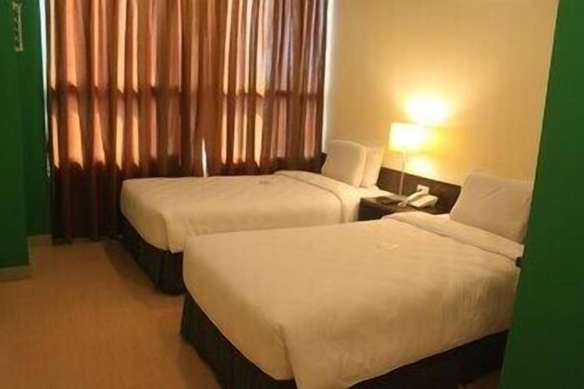 A hotel room with two beds, a nightstand with a lamp, and a curtain.