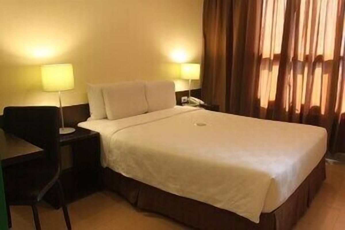 A hotel room with a bed, two bedside lamps, a desk, and a chair.