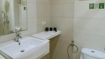 Baño con lavamanos blanco, espejo y retrete. Hay un toallero sobre el inodoro y una repisa con artículos de aseo.