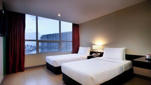 A hotel room with two beds, a nightstand with a lamp, a window with red curtains, and a view of a cityscape. - Go Hotels Plus Mandaluyong (Mandaluyong)