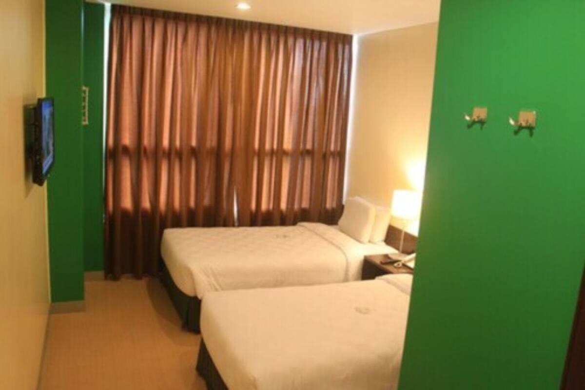 A hotel room with two beds, a television, a curtain, and a green wall.