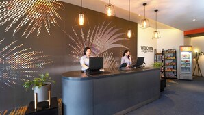 A reception desk with two staff members, a wall with a light pattern, and a G2G sign. - Go Hotels Plus Mandaluyong (Mandaluyong)