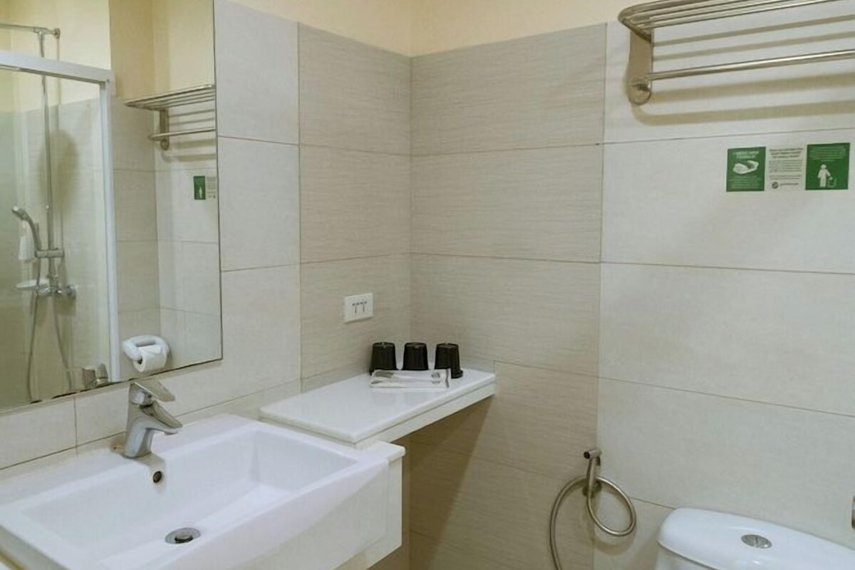 A small, clean bathroom with a white sink, mirror, and toilet. There is a shelf above the sink with toiletries and a towel hanging on the wall.