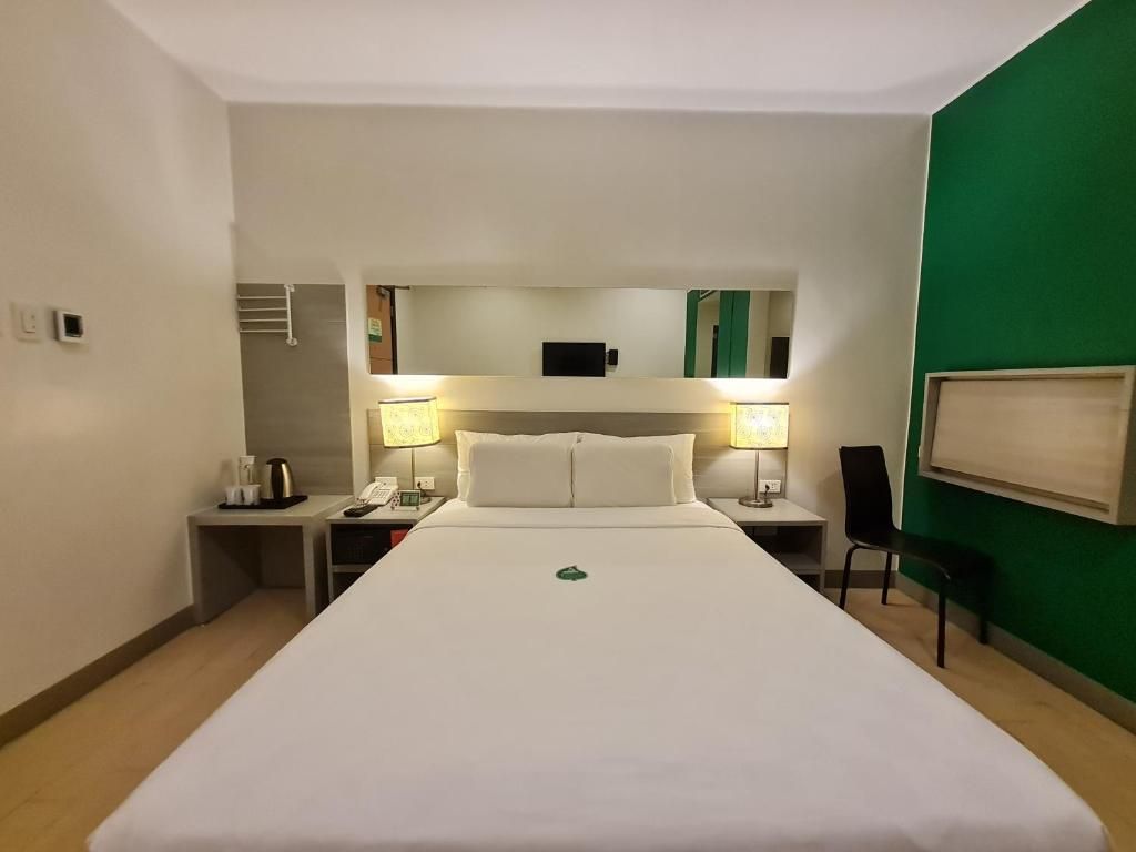 Habitación de hotel con una cama grande, lámparas de noche, un espejo, una silla y una mesita con una tetera.