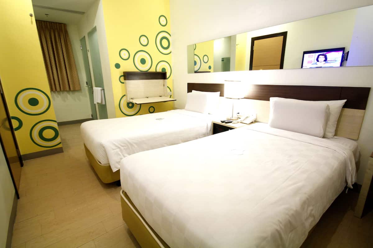 A hotel room with two beds, a mirror, a television, and a small table.