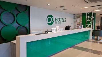 A hotel reception desk with a green and white color scheme, a digital screen, and a sign indicating CCTV in operation.