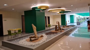 A modern hotel lobby with green walls, a central water feature, and a long corridor with seating areas. - Go Hotels Otis - Manila (Manila)
