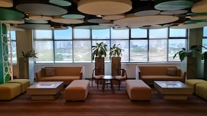 A modern lobby with sofas, ottomans, and a coffee table, large windows with a city view, and decorative ceiling lights. - Go Hotels Otis - Manila (Manila)