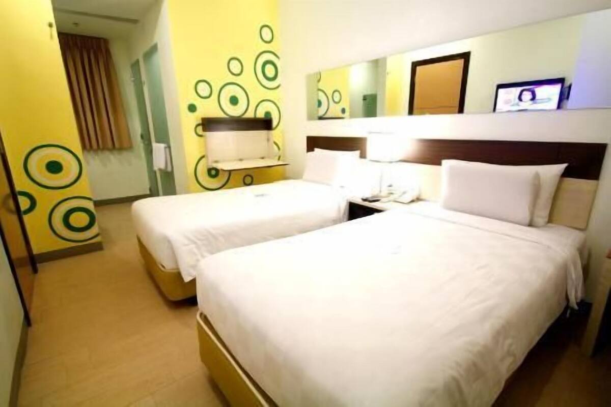 A hotel room with two beds, a bedside table with a lamp, a mirror, and a wall with circular patterns.