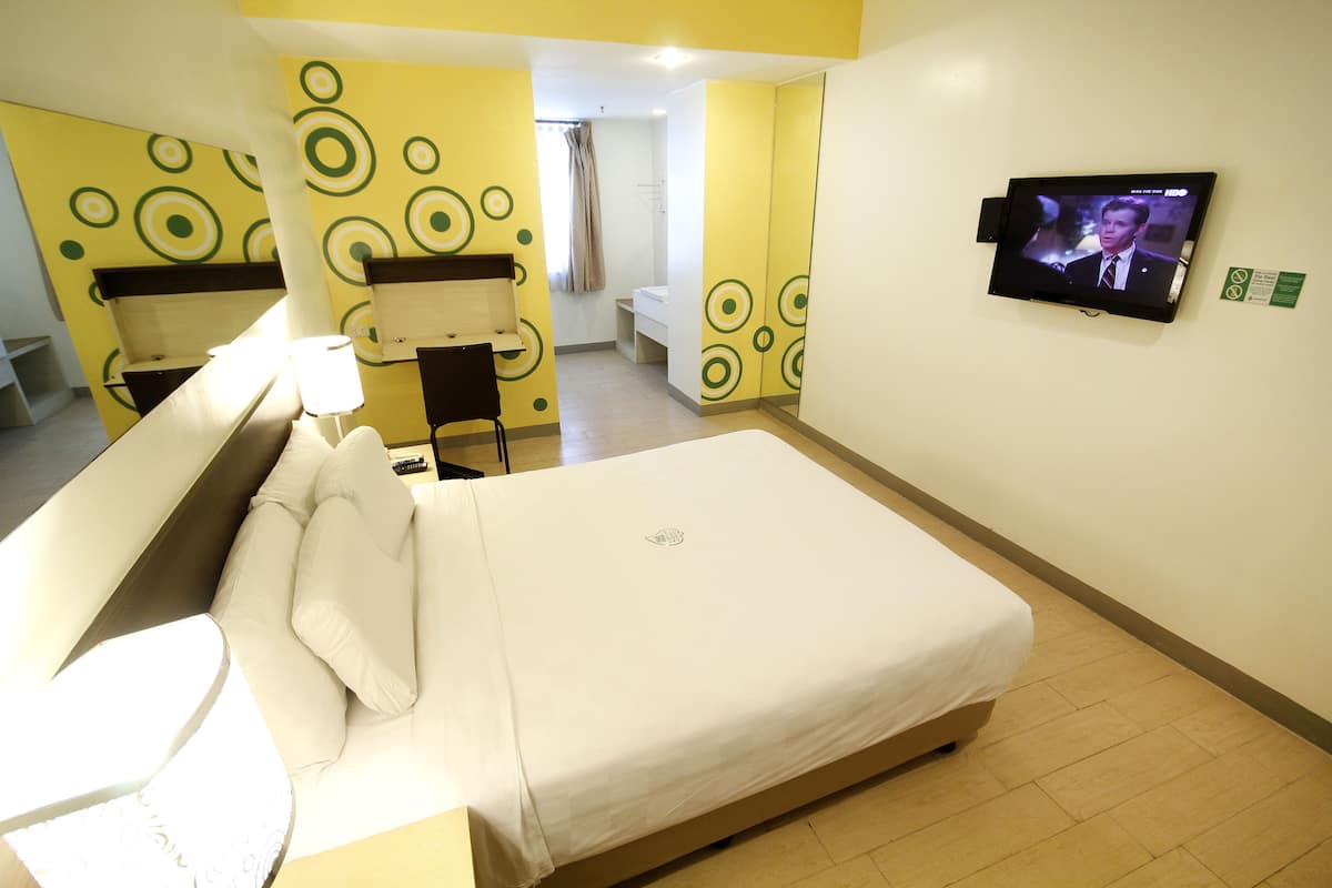 A hotel room with a bed, a TV mounted on the wall, and a bathroom visible through an open door.