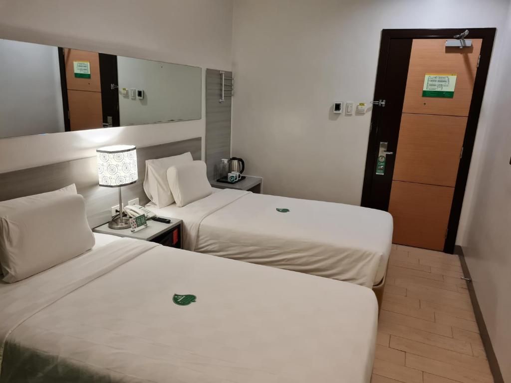 Hotellihuone, jossa on kaksi sänkyä, yöpöytä lampun kanssa, puhelin ja kyltti ovessa.