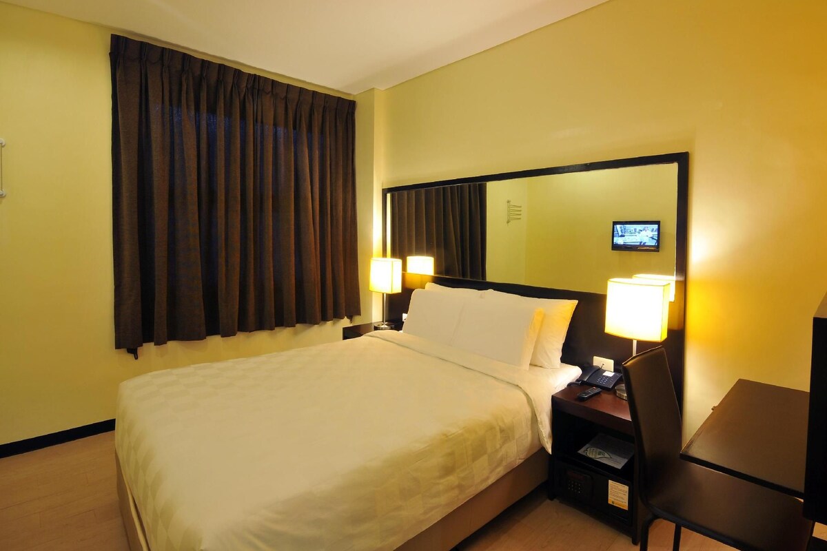 Una habitación de hotel con una cama, lámparas de noche, un escritorio y un televisor.