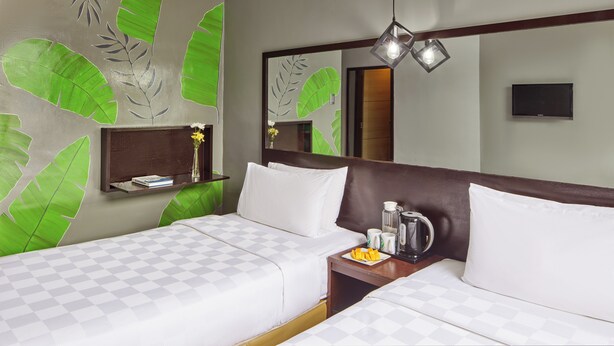 A hotel room with two beds, a nightstand with a coffee maker, a TV, and a large mirror. - Go Hotels Puerto Princesa (Puerto Princesa)