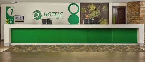A hotel reception desk with a green and white color scheme, a digital screen, and a reception counter.