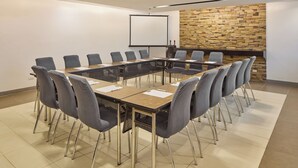 A conference room with a long table, multiple chairs, a projector screen, and a stone wall. - Go Hotels Puerto Princesa (Puerto Princesa)