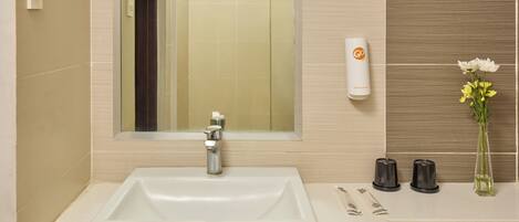 A bathroom with a white sink, a mirror, a hand soap dispenser, and a vase with flowers.