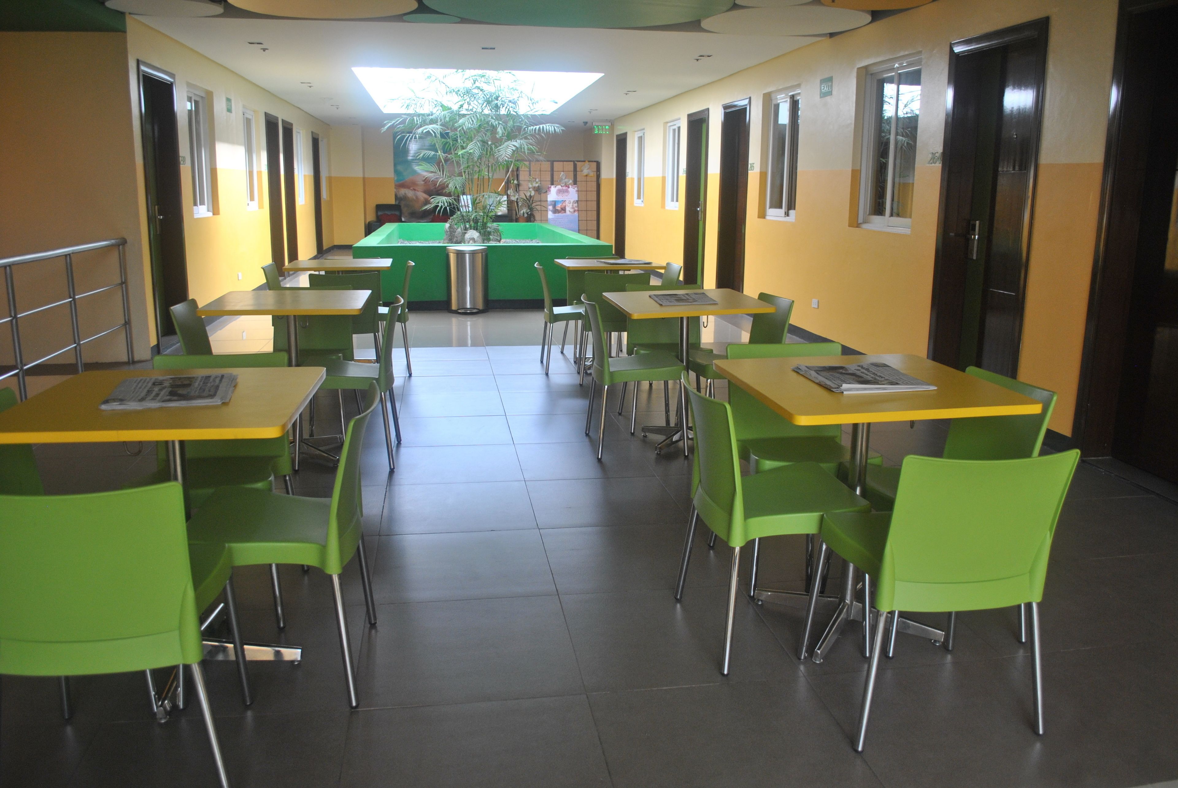 A cafeteria with green chairs and yellow tables, arranged in rows with a central serving area.