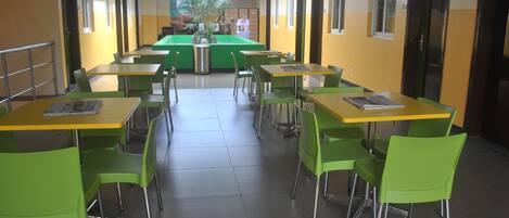A cafeteria with green chairs and yellow tables, arranged in rows with a central serving area.