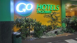 A hotel entrance with a 'Go Hotels Tacloban' sign, a planter with various plants, and a trash bin. - Go Hotels Tacloban (Tacloban)