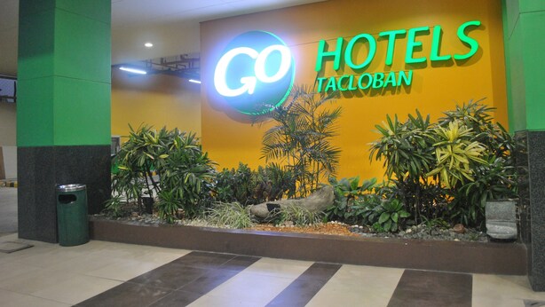 A hotel entrance with a sign reading "GO HOTELS TACLOBAN" and a well-maintained outdoor area with plants and a trash bin. - Go Hotels Tacloban (Tacloban)
