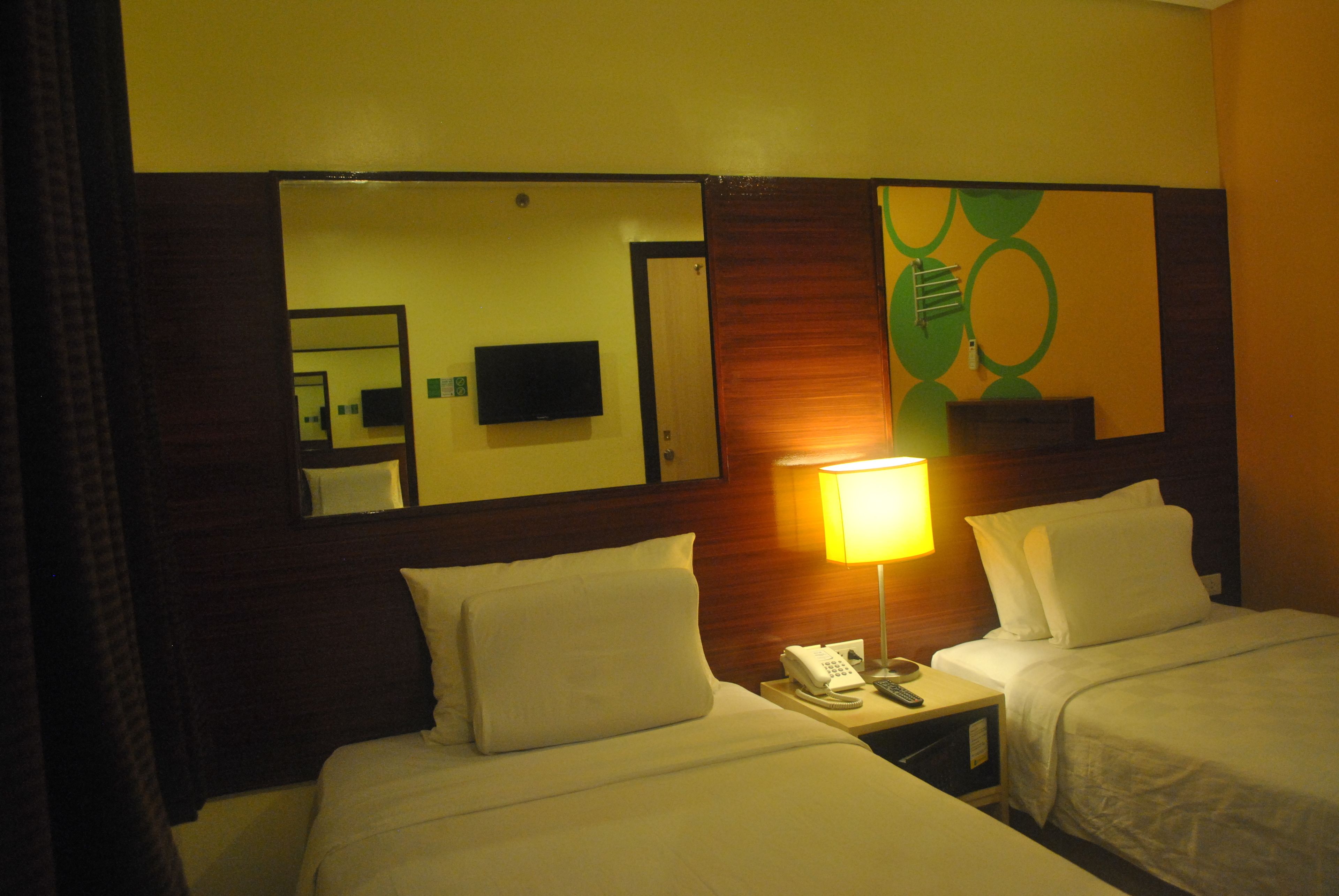 A hotel room with two beds, a bedside telephone, a lamp, and a mirror reflecting the room.