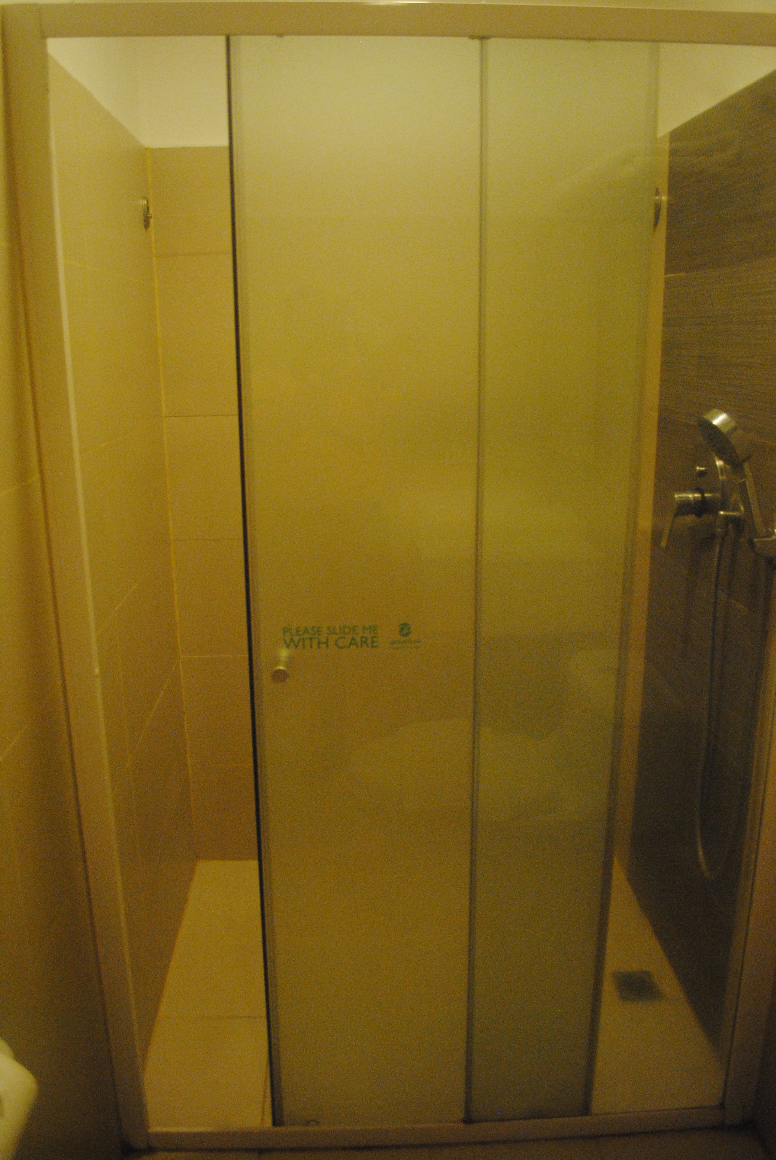 A glass-enclosed shower stall with a door marked "Please use me with care."