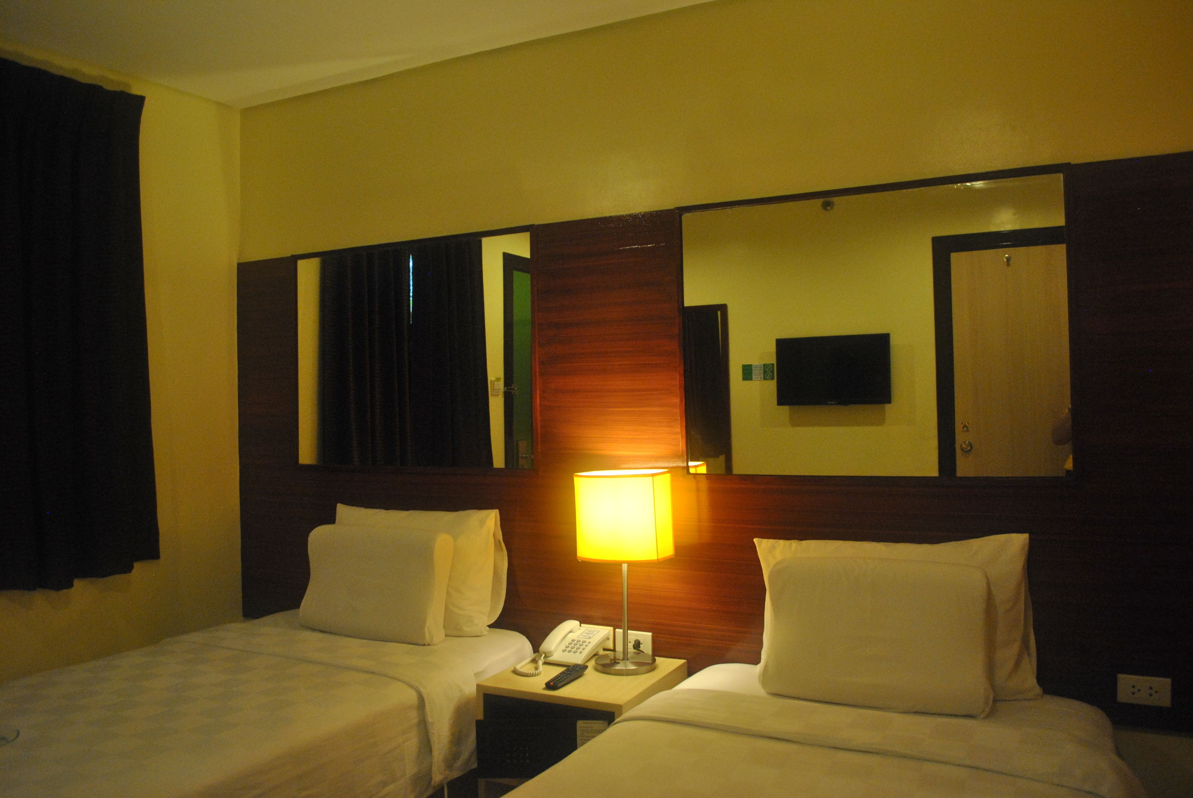 A hotel room with two beds, a nightstand with a lamp, a phone, and a mirror above the beds.