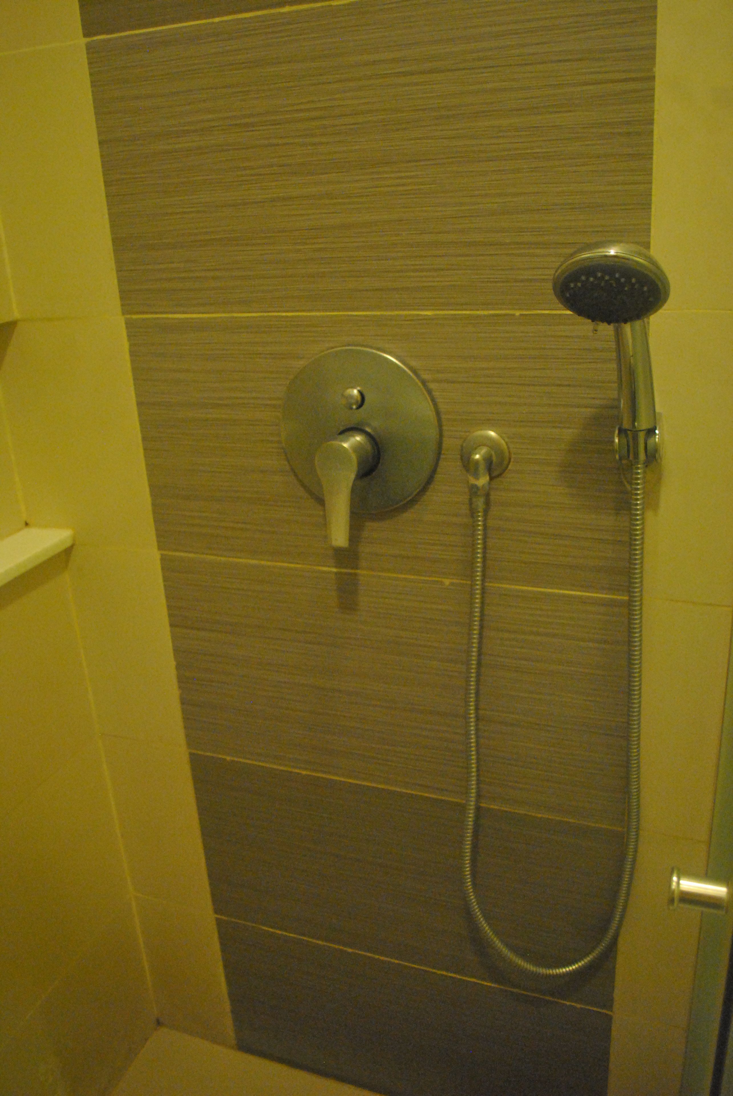 A shower with a handheld showerhead and a wall-mounted faucet.