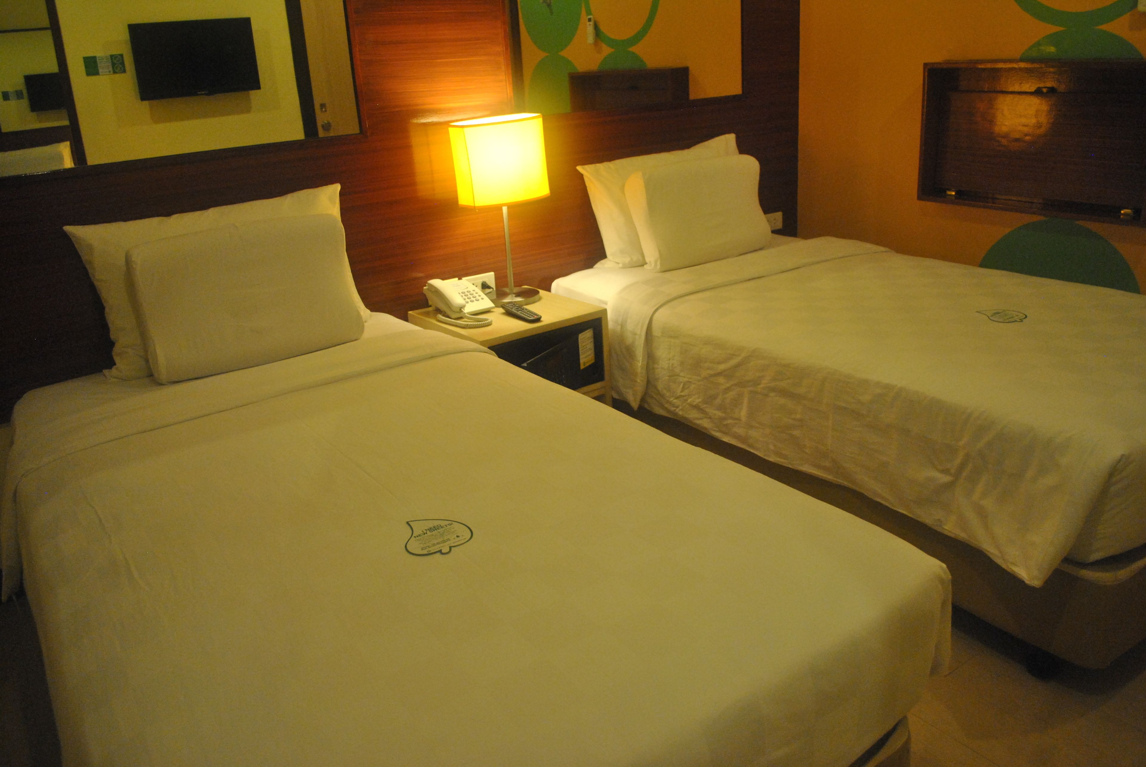 A hotel room with two single beds, a nightstand with a lamp, a phone, and a TV mounted on the wall.